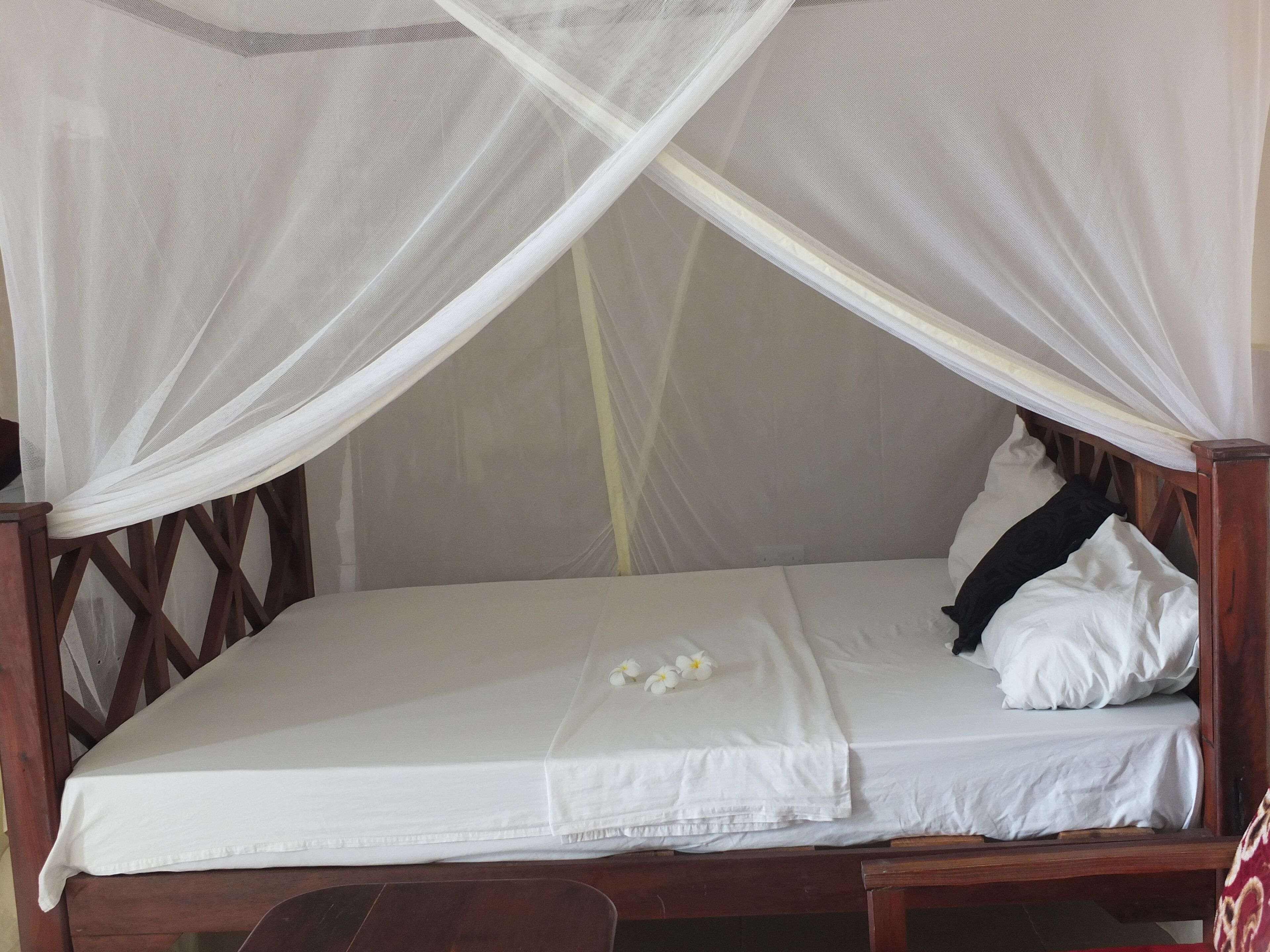 Una cama con estructura de madera, ropa de cama blanca y un mosquitero.