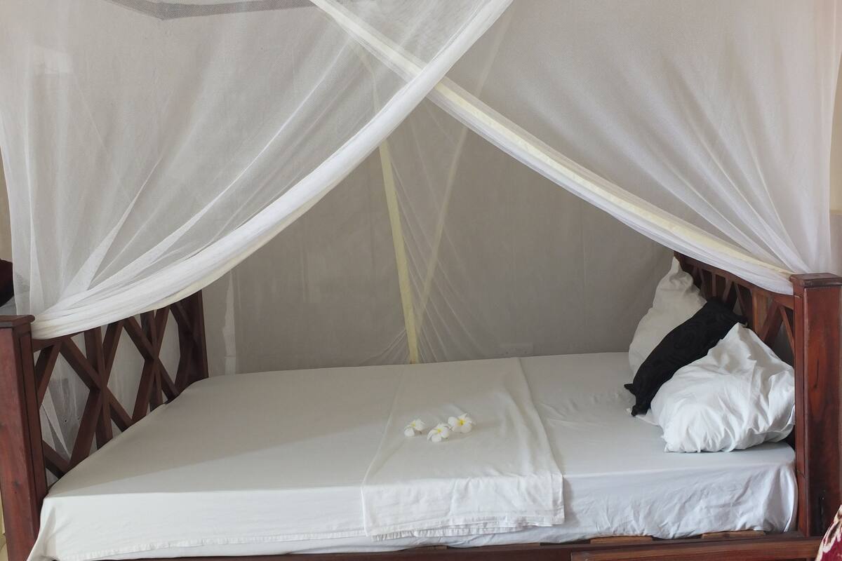 Ein Bett mit Holzrahmen, weißer Bettwäsche und einem Moskitonetz.