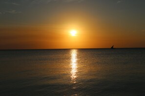 Un coucher de soleil sur une mer calme, avec un voilier à l'horizon.