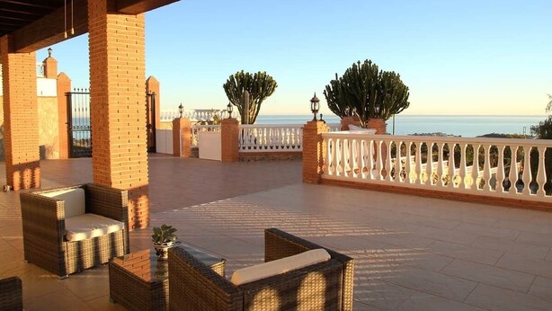 A covered outdoor area with wicker furniture, a white railing, and cacti. - Villa El Palomar Azul (Los Puertas)