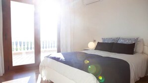 A bedroom with a bed, a nightstand, a lamp, and a view of a balcony. - Villa El Palomar Azul (Los Puertas)