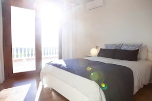 Een slaapkamer met een bed, nachtkastje, lamp en uitzicht op een balkon.