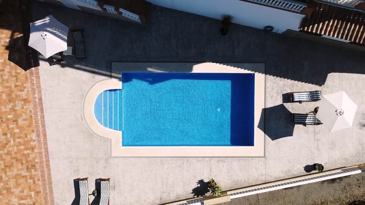 Luchtbeeld van een zwembad met ligbedden en parasols, omgeven door een betegeld terras.
