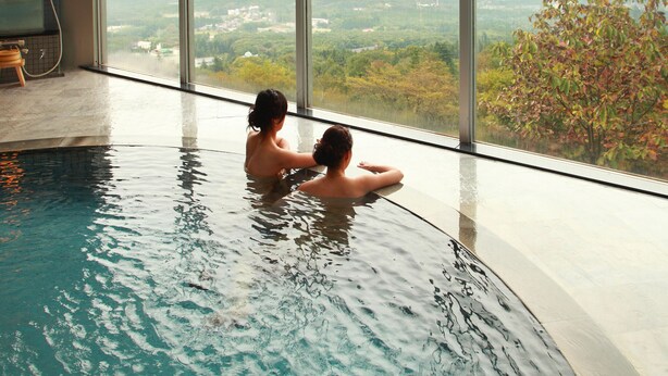 A large indoor swimming pool with a view of a cityscape and mountains. - ikaho shinki (Shibukawa)
