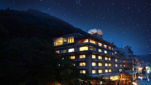 A multi-story hotel with illuminated windows and a balcony, surrounded by trees and a night sky with stars. - ikaho shinki (Shibukawa)