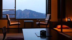 A room with a large window, two chairs, a small table, and a red pillow. - ikaho shinki (Shibukawa)