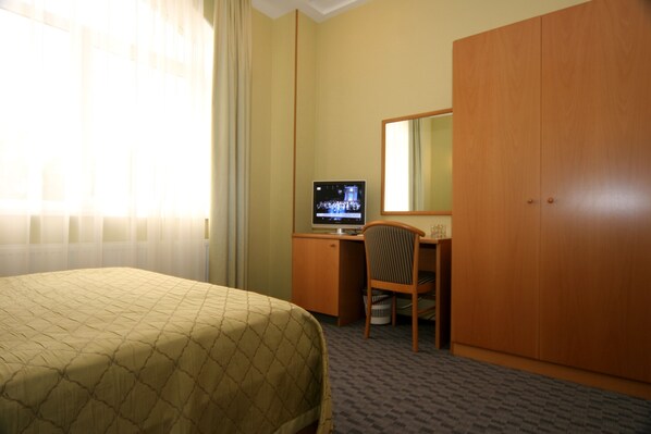 A hotel room with a bed, a desk, a television, and a wardrobe.