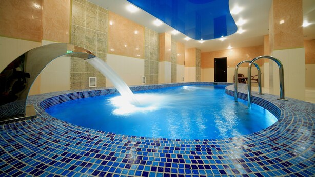 Una piscina interior con suelo y paredes de azulejos azules, una fuente de agua y una puerta al fondo.