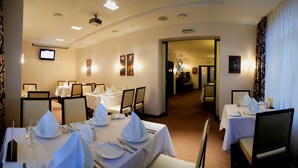 Un comedor de hotel con mesas dispuestas para una comida, una pantalla de televisión y cuadros en las paredes.