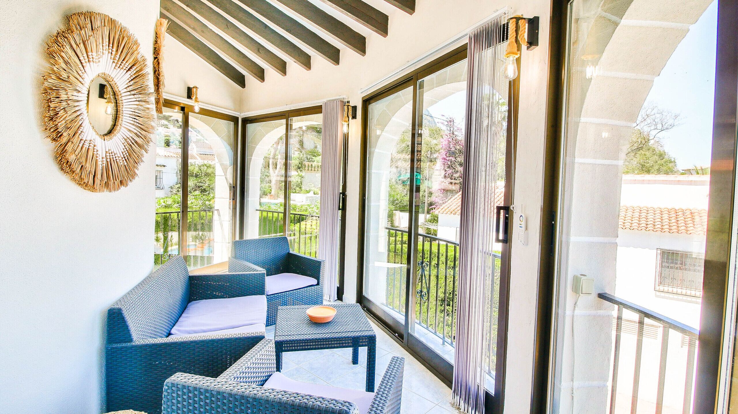 A balcony with wicker furniture, a decorative mirror, and large windows with curtains.