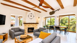 A spacious living area with a stone fireplace, modern furniture, and large windows offering a view of greenery.