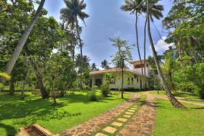 Un jardin tropical avec un sentier de pierres menant à un bâtiment doté d’un toit en tuiles.