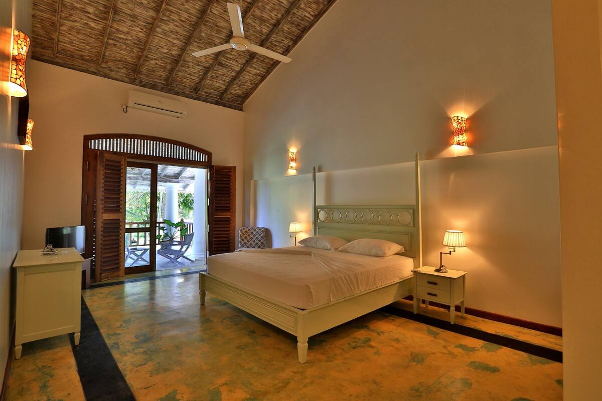 Quarto com cama, mesas de cabeceira, ventilador de teto e vista para o exterior.
