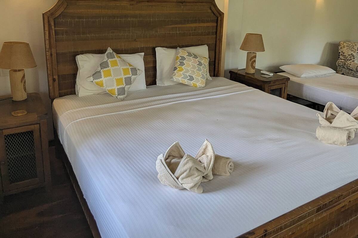 Uma cama grande com cabeceira de madeira, duas mesas de cabeceira com luminárias e uma mesinha com abajur.