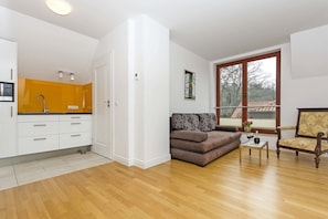 Relax in this stylish living space with a kitchen, sofa, and coffee table, offering a view of the outside through the window.