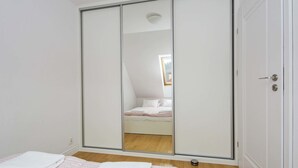 Une chambre avec un placard à porte coulissante, un lit avec une literie blanche et une petite fenêtre.