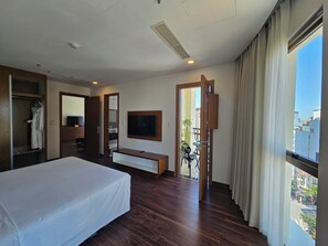 A hotel room with a bed, a TV, a wardrobe, a mirror, and a balcony with a view of the city. - Tamarind Hotel Da Nang (Da Nang)