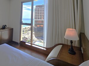 A hotel room with a bed, a desk, a lamp, and a view of the cityscape through a large window. - Tamarind Hotel Da Nang (Da Nang)