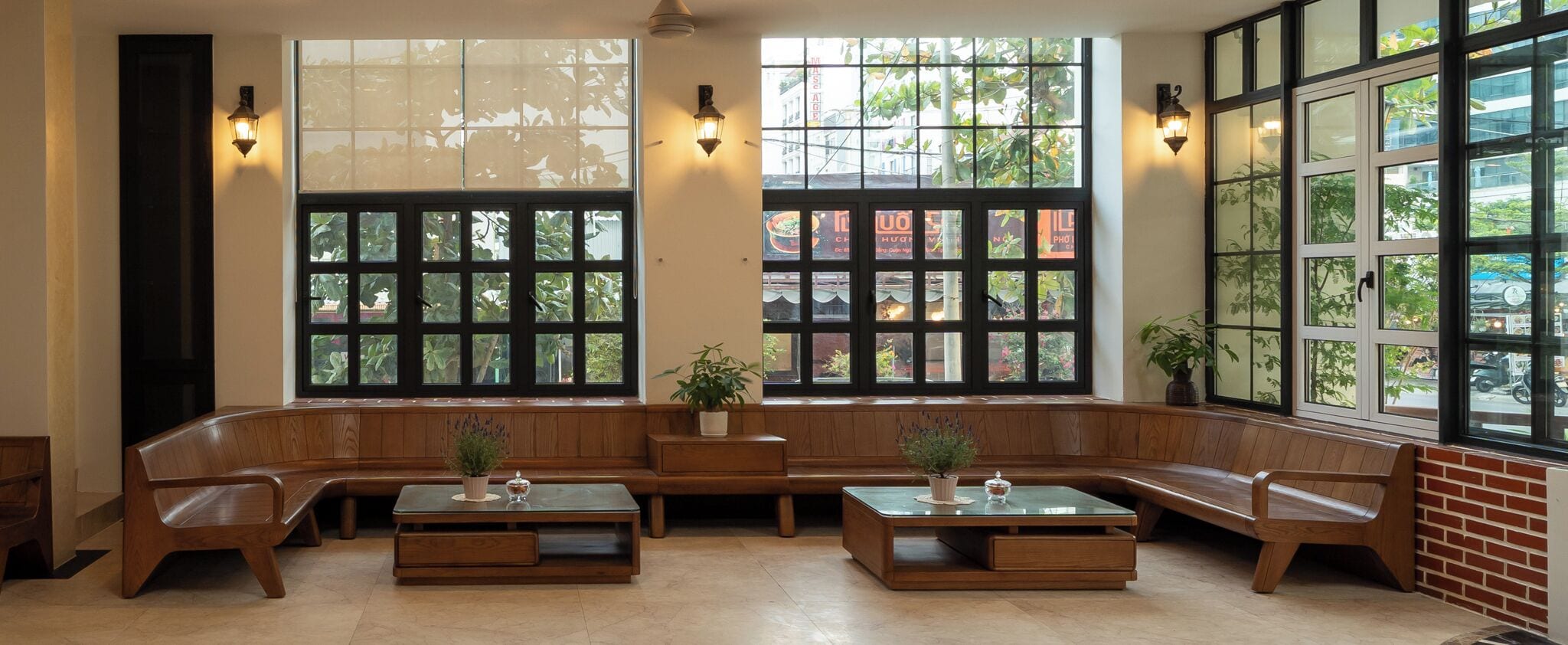 A seating area with wooden benches and tables, large windows with grid patterns, and wall-mounted lights.
