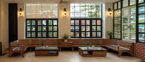 A seating area with wooden benches and tables, large windows with grid patterns, and wall-mounted lights.