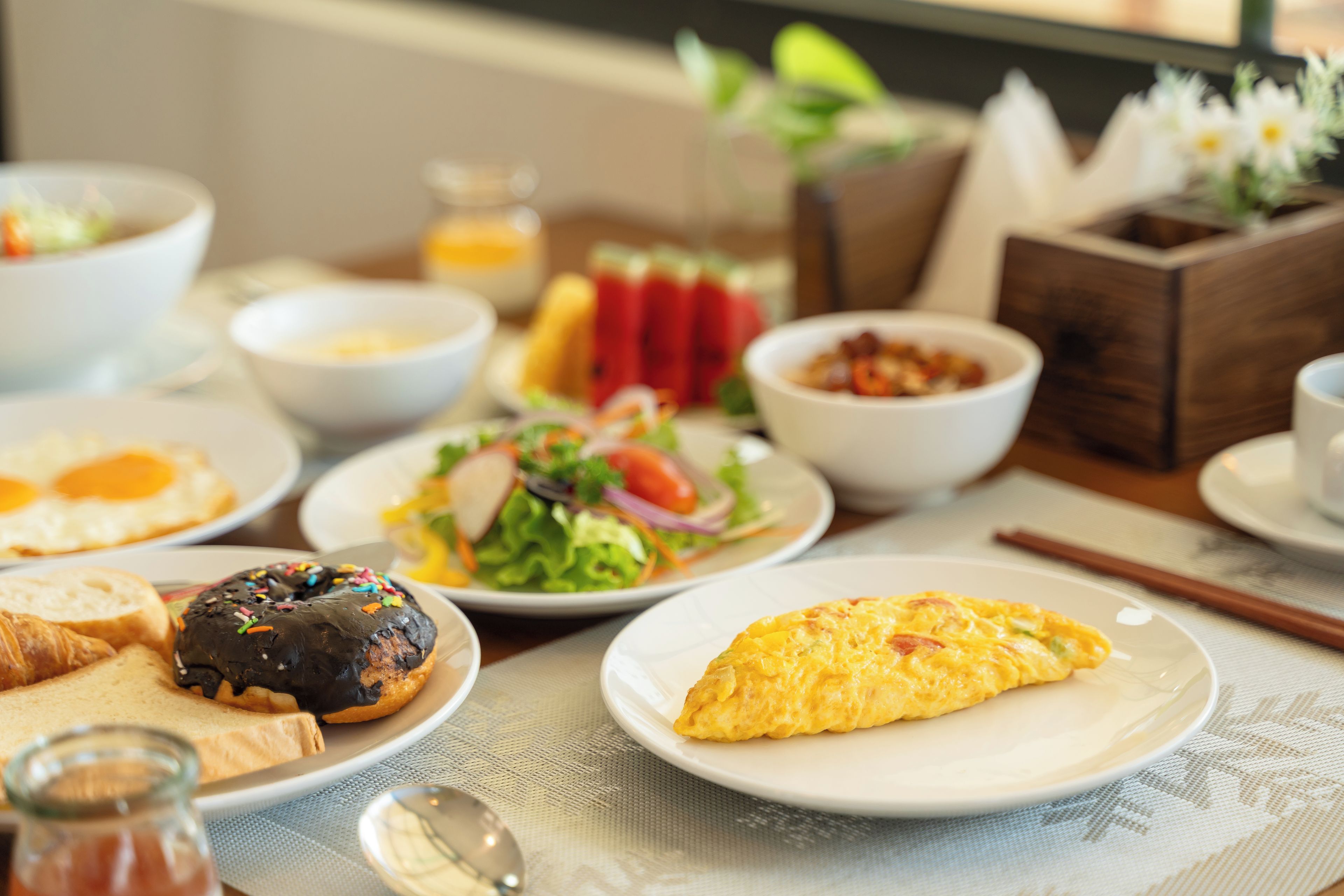 Desayuno con diversos platos, incluyendo huevos, tostadas, una ensalada y un bol de fruta.
