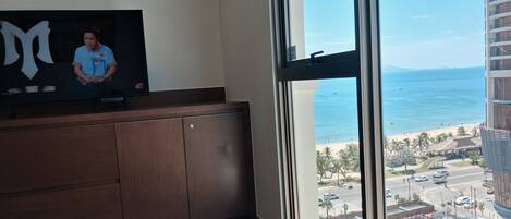 A room with a large window overlooking a beach and a cityscape.