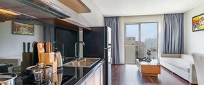 A modern kitchen with a sink, stove, and cabinets, a dining area with a table and chairs, and a living room with a sofa and a window with curtains. - Tamarind Hotel Da Nang (Da Nang)