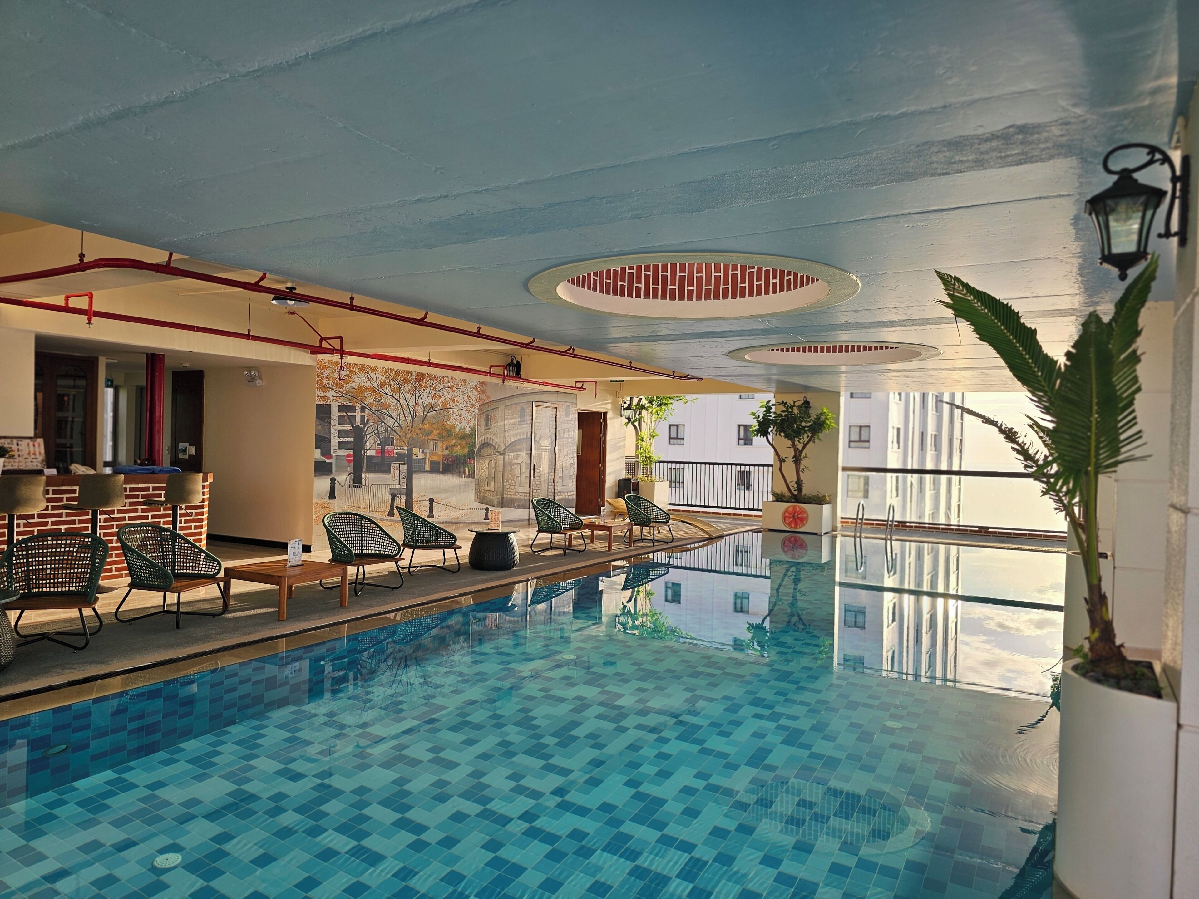 Una piscina interior con un diseño de baldosas a cuadros, rodeada de sillones de descanso y un mostrador de recepción.