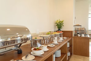 A buffet setup with various food items, a coffee station, and a plant in the background. - Tamarind Hotel Da Nang (Da Nang)