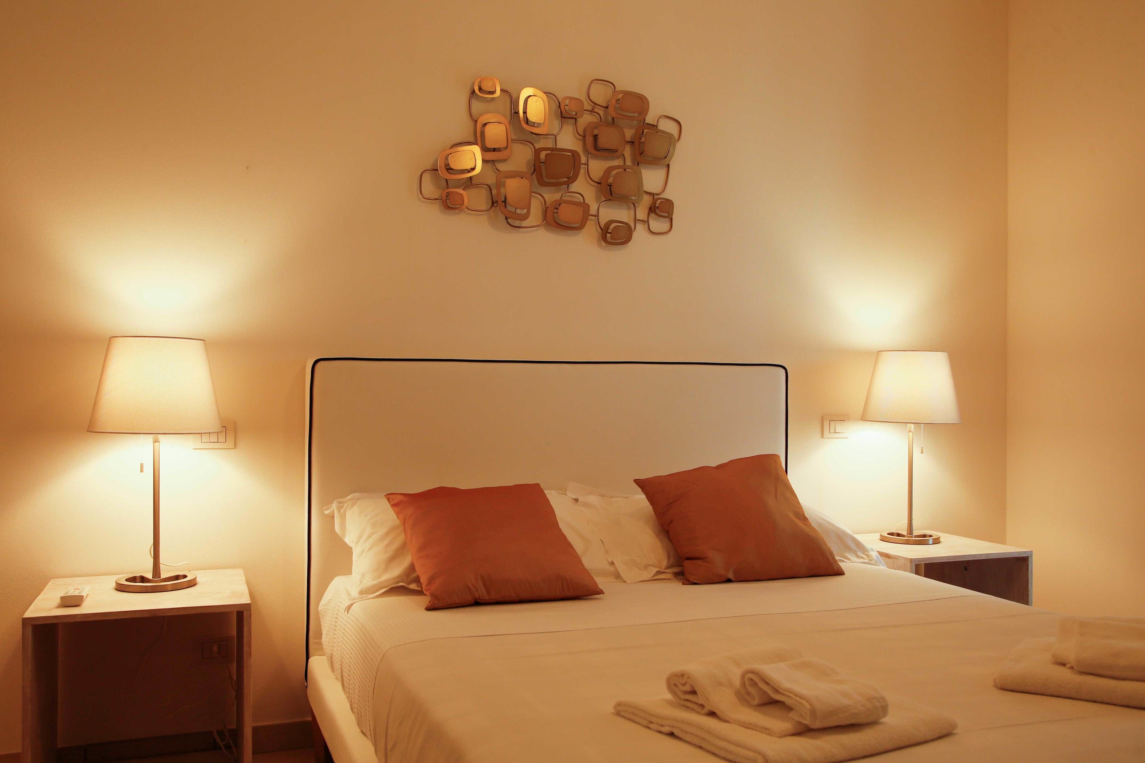Ein ordentlich bezogenes Bett mit zwei Kissen, zwei Nachttischlampen, einem Wandbild und gefalteten Handtüchern.