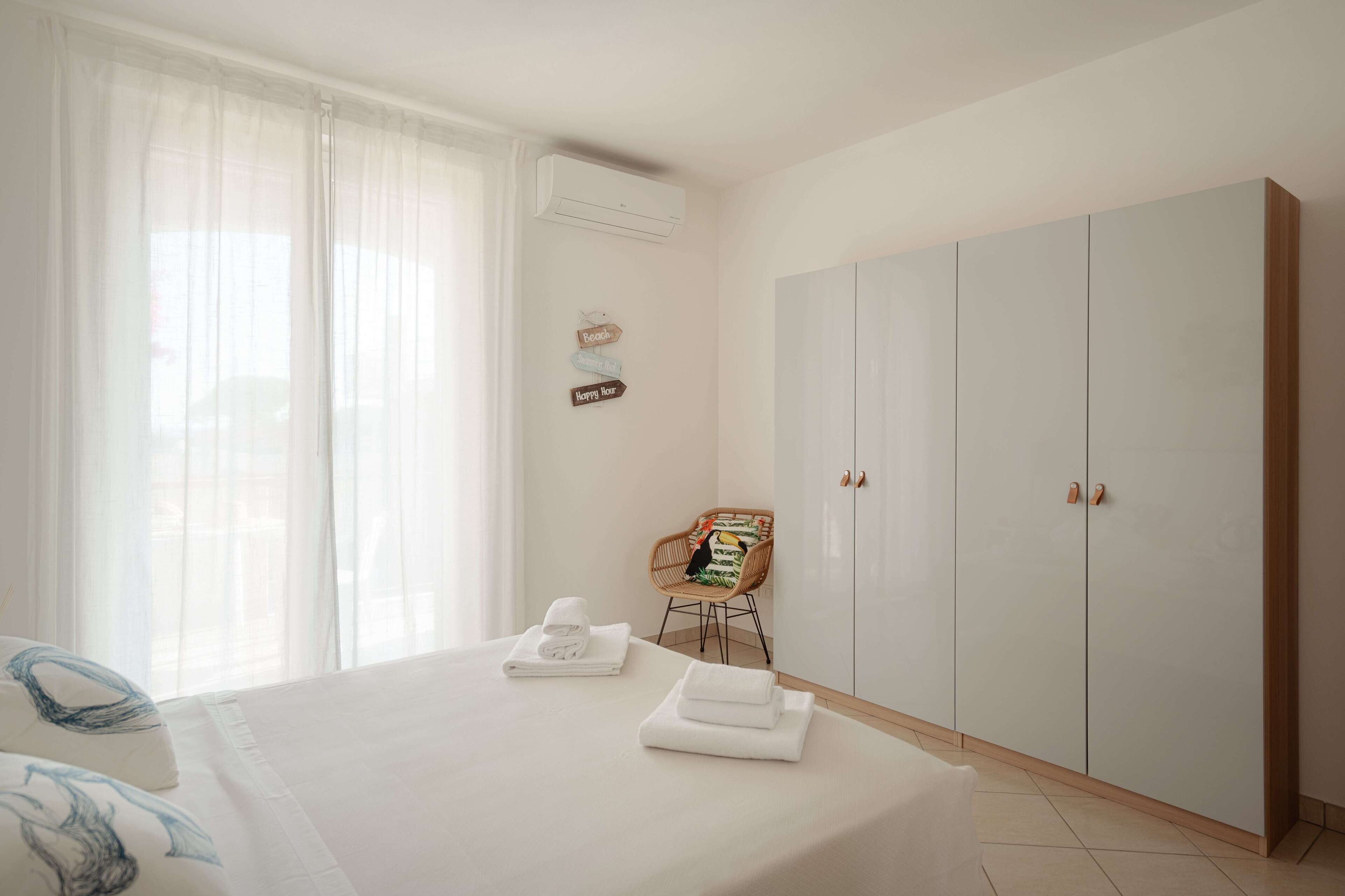 A hotel room with a bed, a chair, a wardrobe, and a wall-mounted air conditioner.