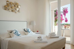 Habitación de hotel con cama, almohadas, mesita de noche, lámpara y vista a flores rosadas a través de una puerta de balcón.