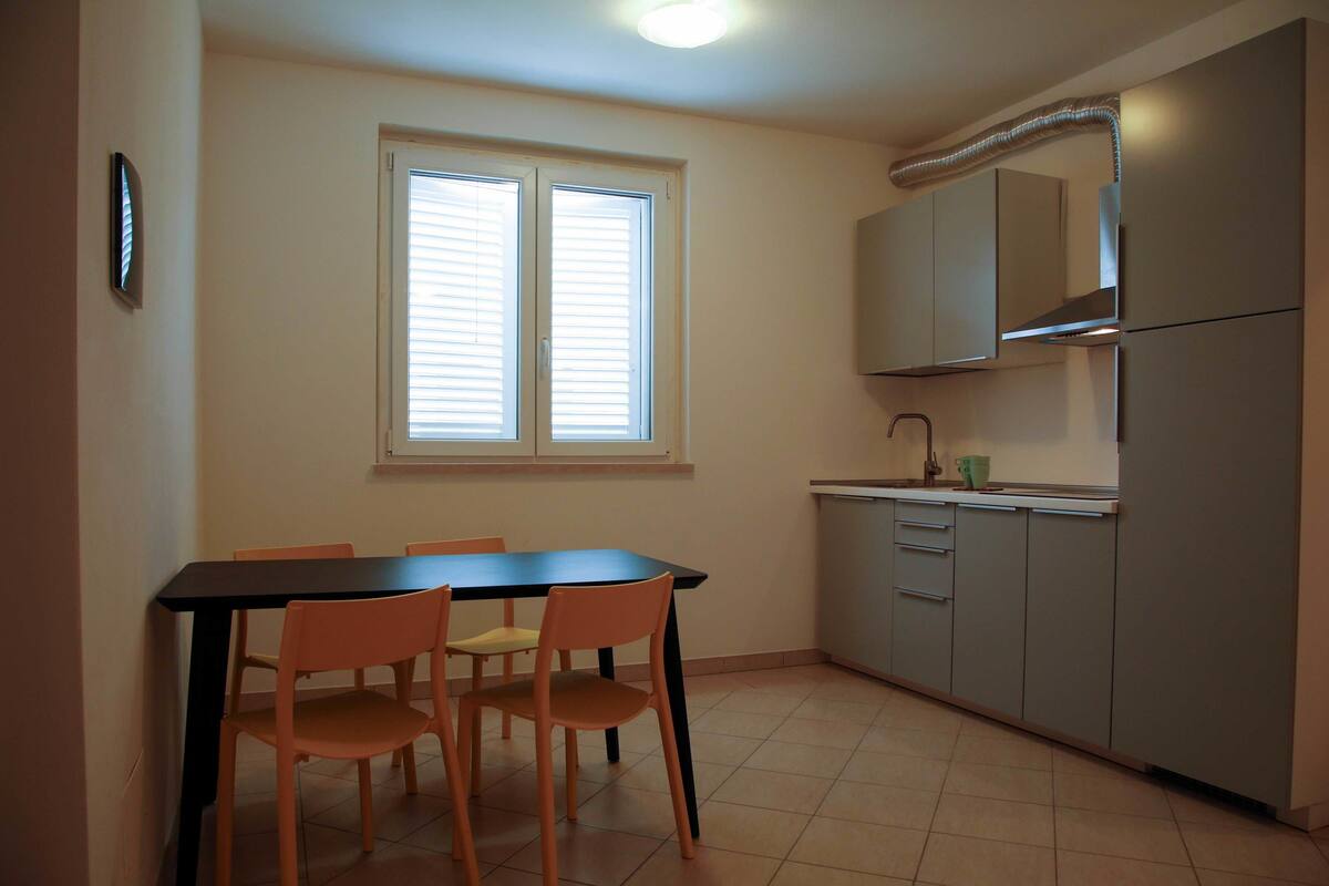 Une cuisine avec une table et des chaises, une fenêtre avec des stores et un four encastré.