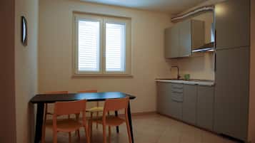 Una cocina con una mesa de comedor y sillas, una ventana con persianas y un horno empotrado.