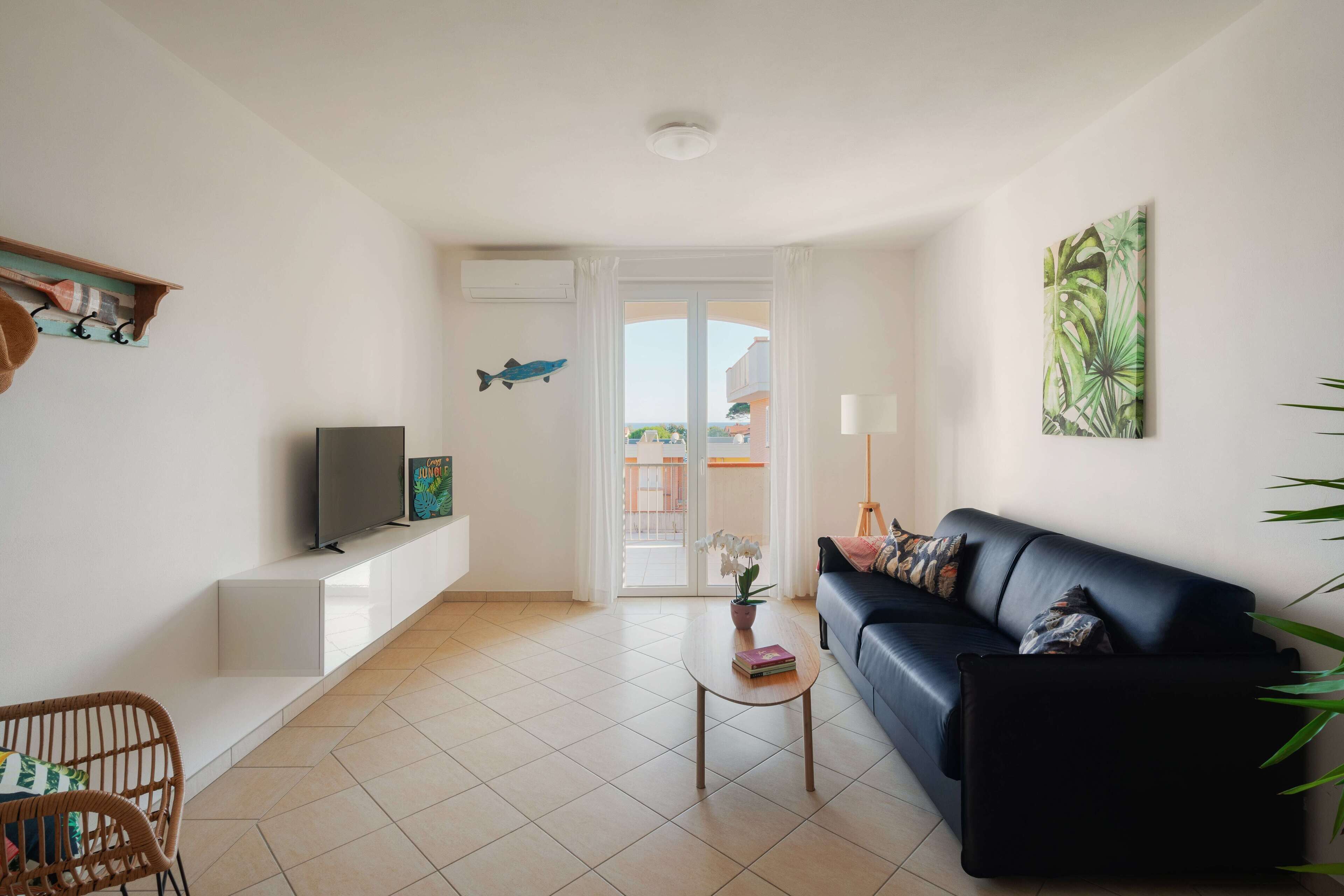A modern living room with a black leather sofa, a flat-screen TV, a coffee table, and a potted plant.