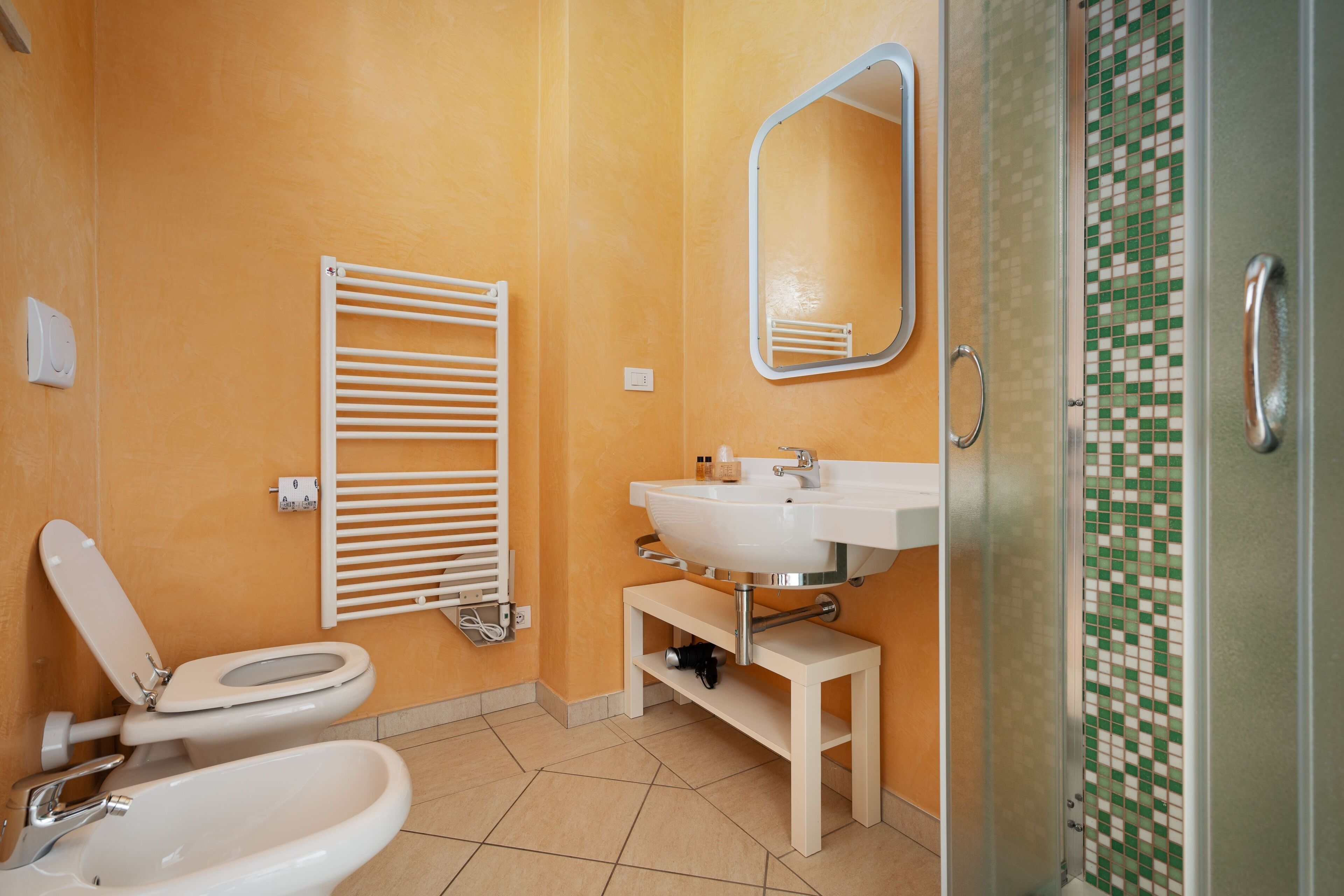 A bathroom with a toilet, bidet, sink, and a shower with a tiled wall.