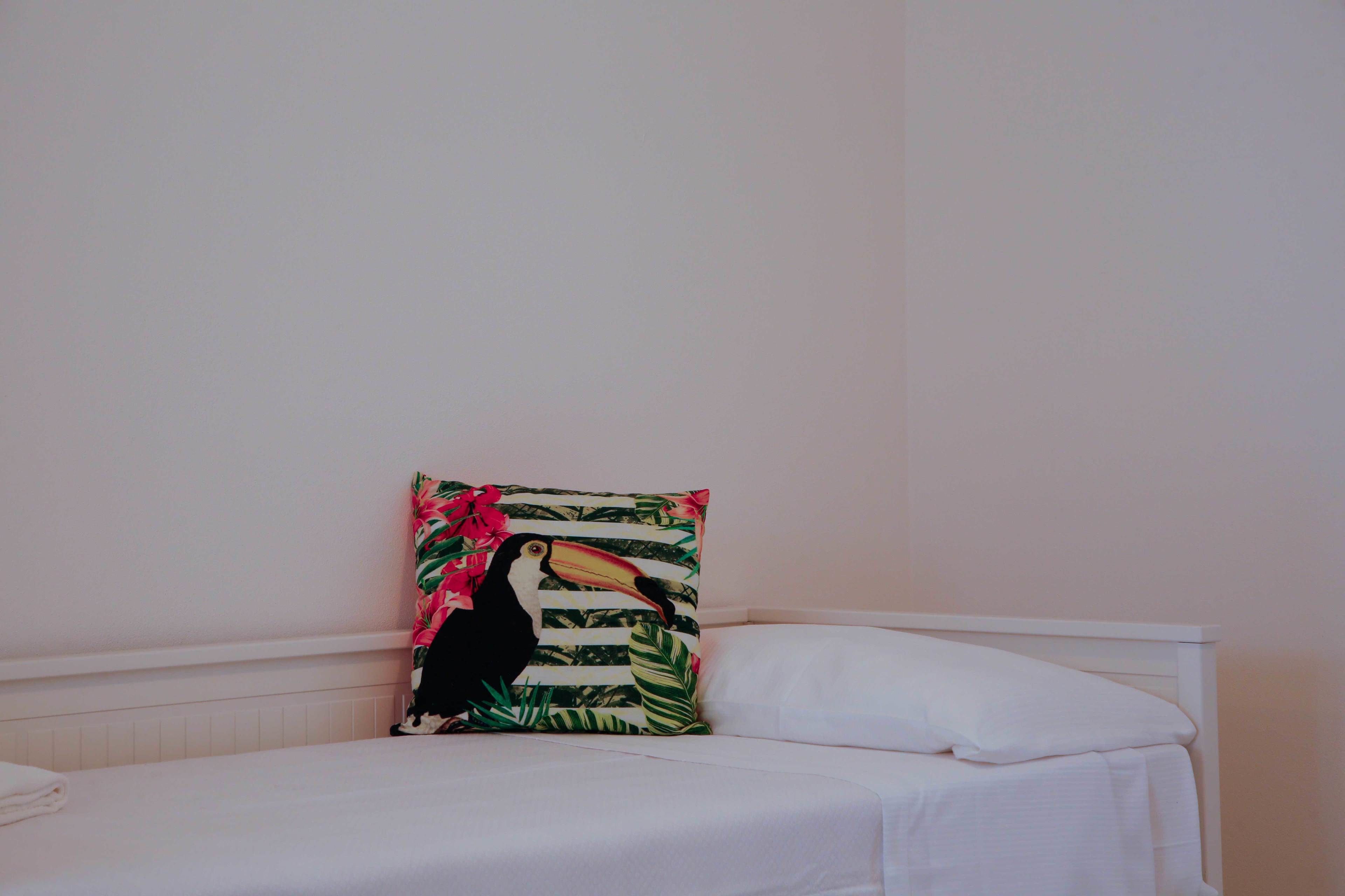 A bed with white bedding and a single pillow with a tropical animal print.