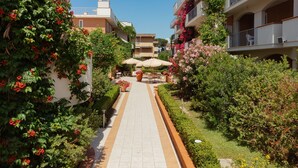 A pathway leading to a courtyard with outdoor seating and lush greenery. - I Cinque Pini (Follonica)