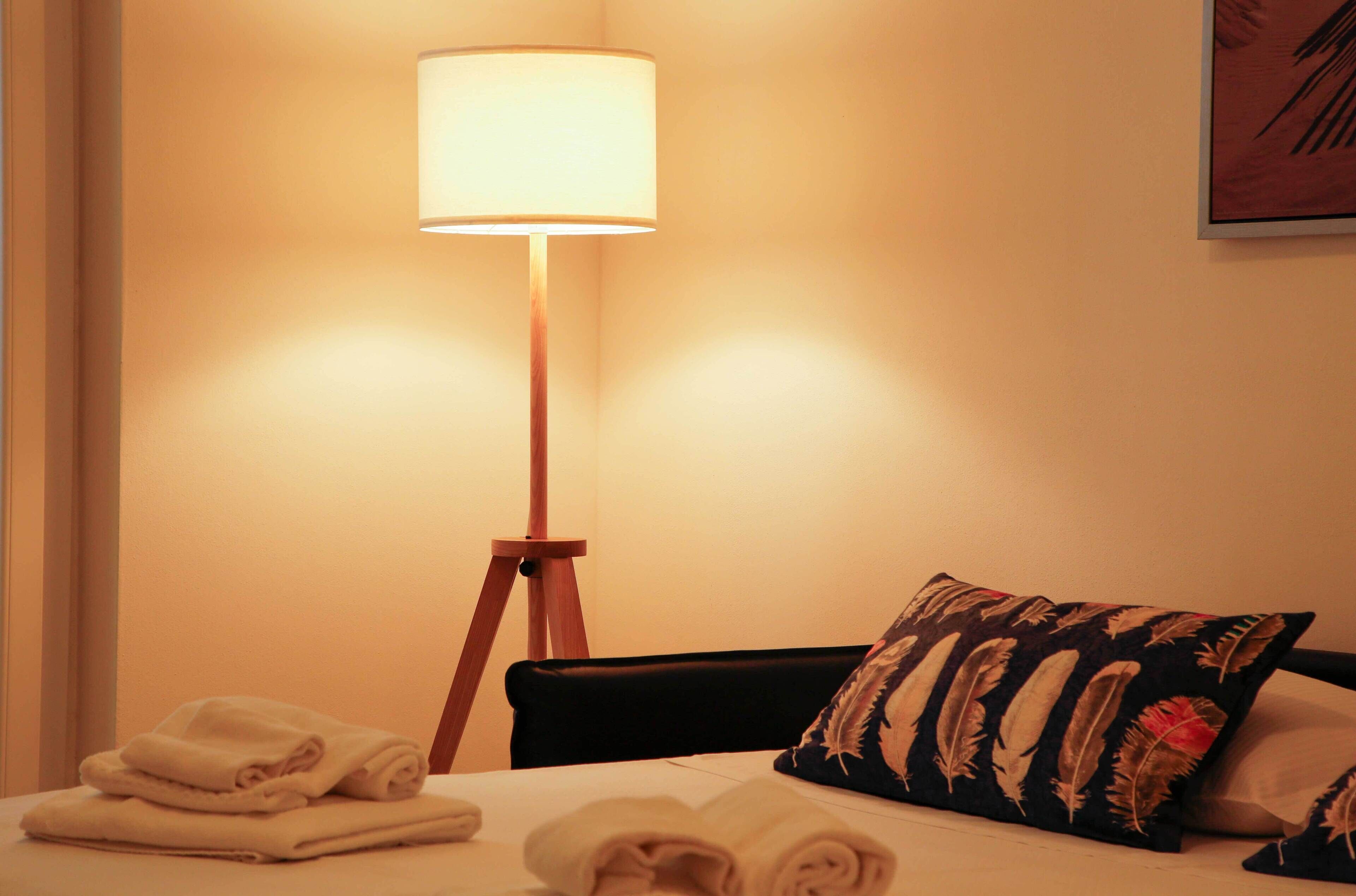 A neatly made bed with folded towels, a standing floor lamp, and a decorative pillow.