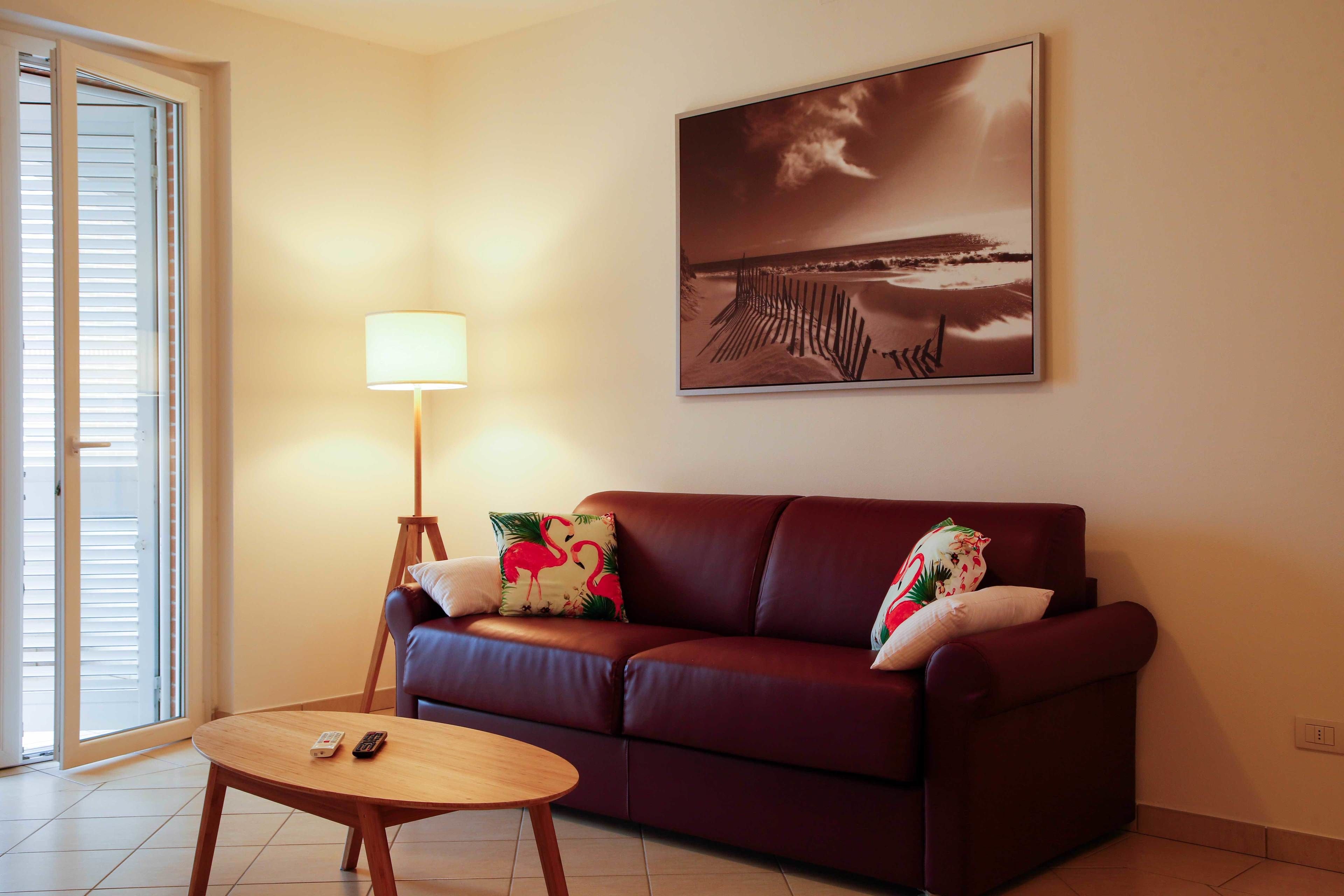 A living room with a brown sofa, a wooden coffee table, a lamp, and a beach scene painting on the wall.