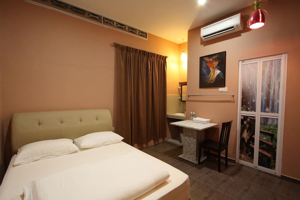 A hotel room with a bed, a desk, a chair, an air conditioner, and a painting on the wall.