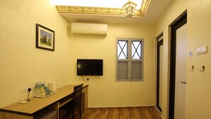 A room with a wooden desk, a television, an air conditioner, and a window with a decorative grille. - Shamrock Guest House II (Ipoh)