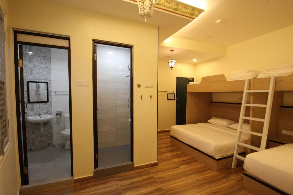 A hotel room with a bathroom, a bed, and a bunk bed.