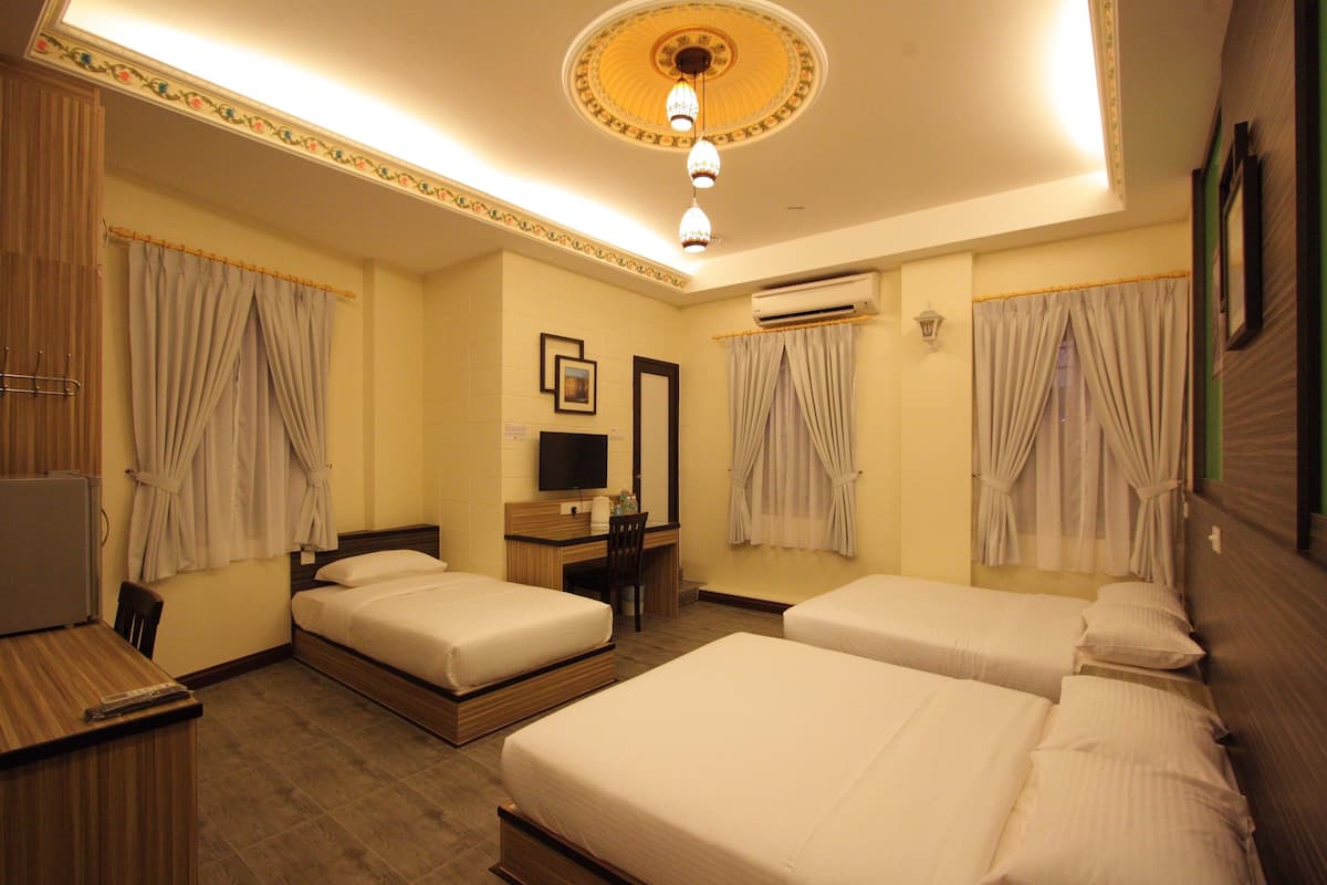 A hotel room with two beds, a desk, a chair, a television, and an air conditioning unit.