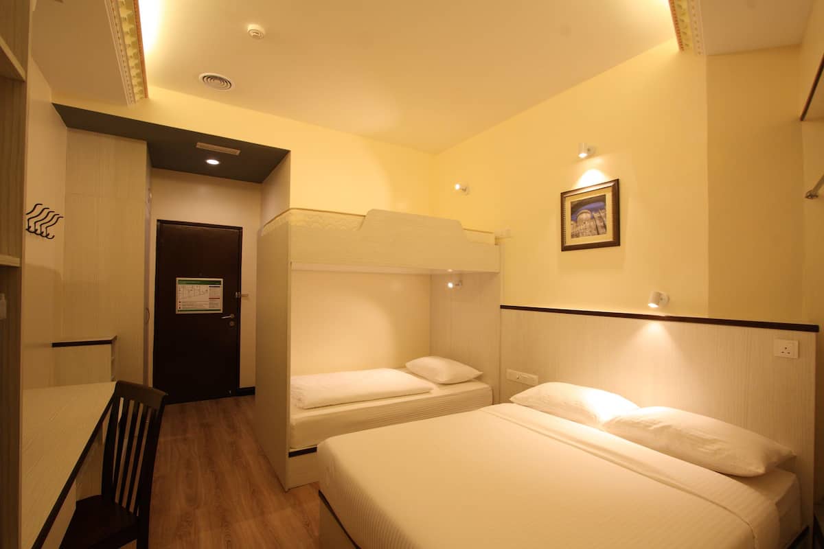 A hotel room with a bunk bed, a single bed, a desk with a chair, and a door with a sign.