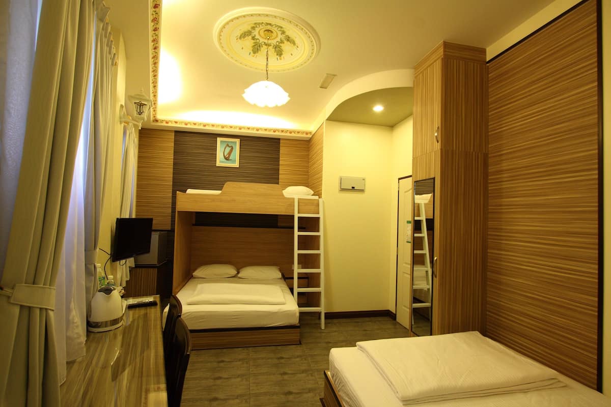 A hotel room with a bunk bed, a desk with a lamp, a television, and a wardrobe.
