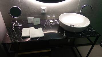 Un baño con lavabo de mármol negro, un espejo redondo, una toalla y un pequeño neceser sobre el mostrador.