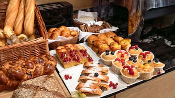 A buffet with various breads, pastries, and fruit-topped desserts.