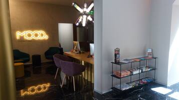Un interior moderno con un mostrador de recepción, dos sillas, una estantería con revistas y un letrero de neón que dice "MOOD".