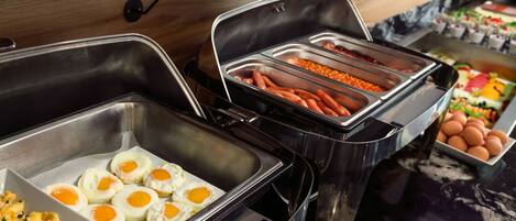 A buffet with various food options including eggs, macaroni, and vegetables.
